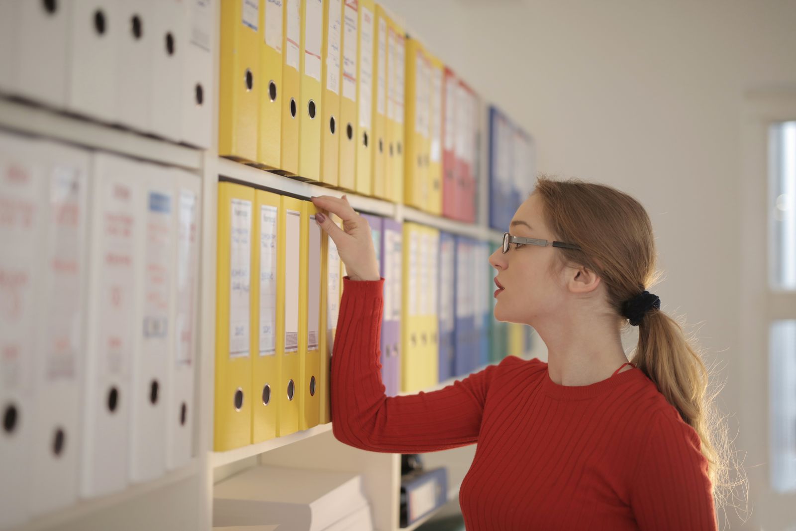 Bookkeeper pulling a labeled binder from a shelf of organized financial records