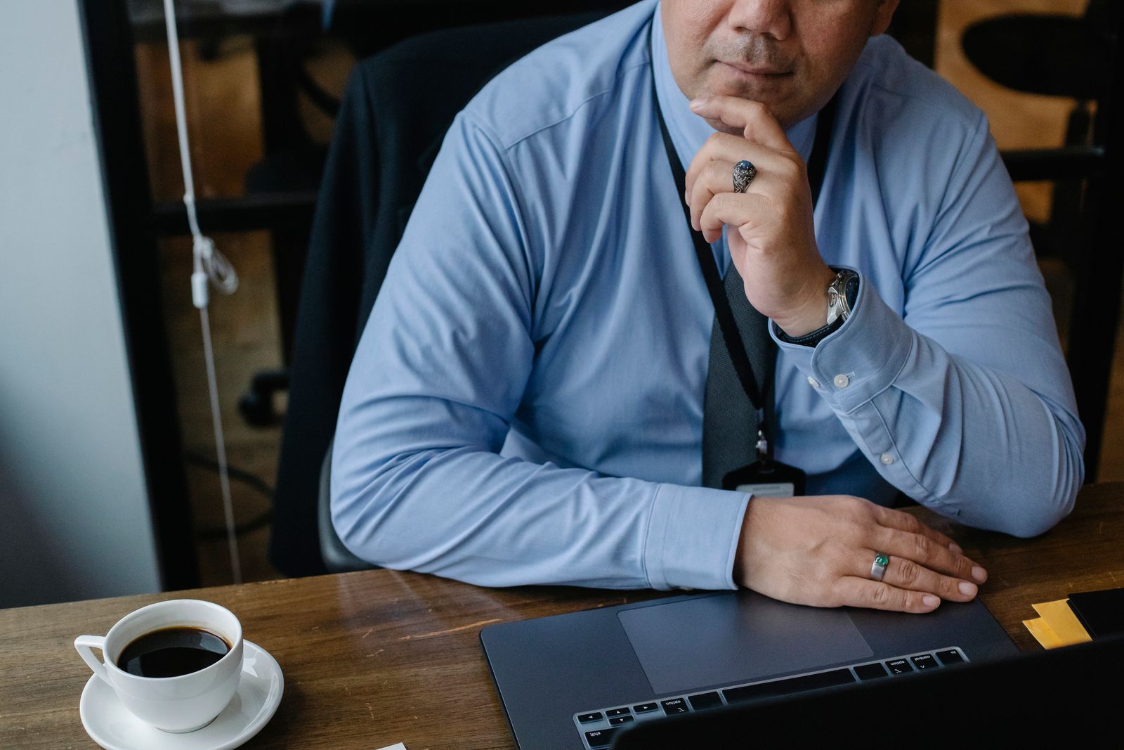 Business owner in a blue shirt seated at a desk with a laptop and coffee, thinking through a decision